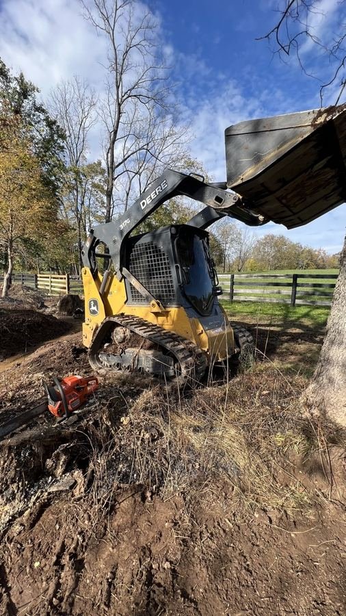 John Deere 317G with bucket raised clearing brush along a fence line